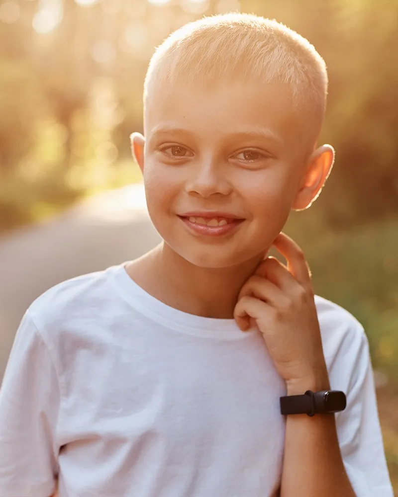 young boy with short hair smiling in the summer