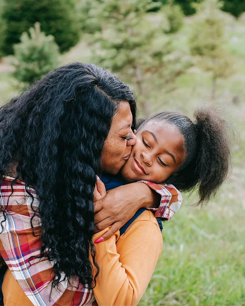 Mom kissing her adolescent child on the cheek in the park