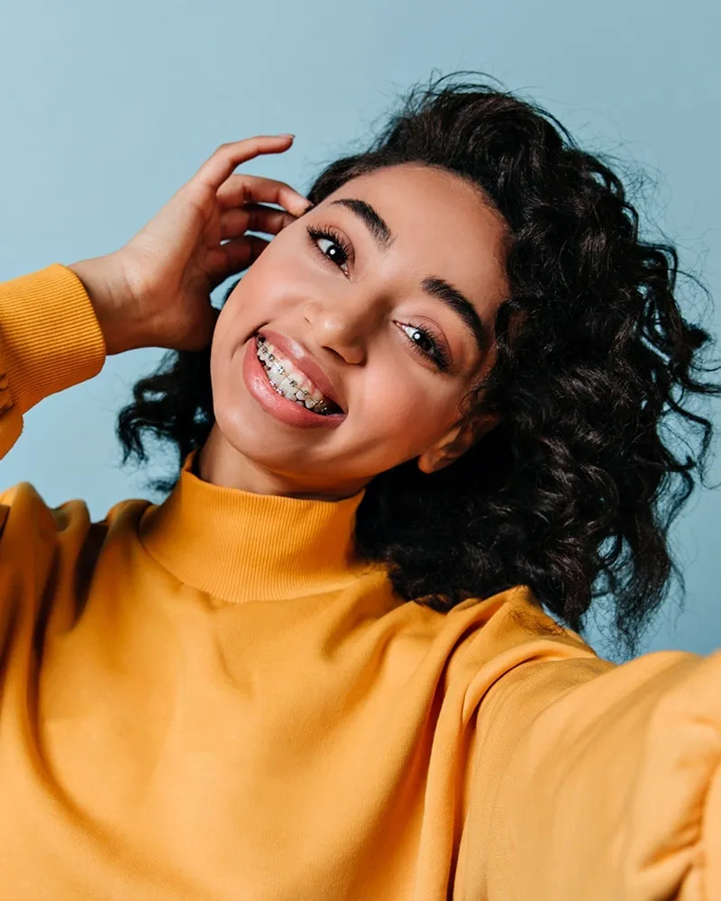 Girl with braces and mustard yellow shirt smiling at camera