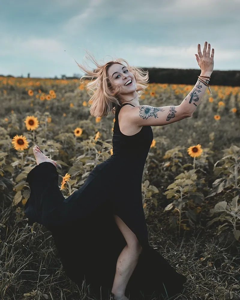 Girl with tattoos running in a field of sunflowers